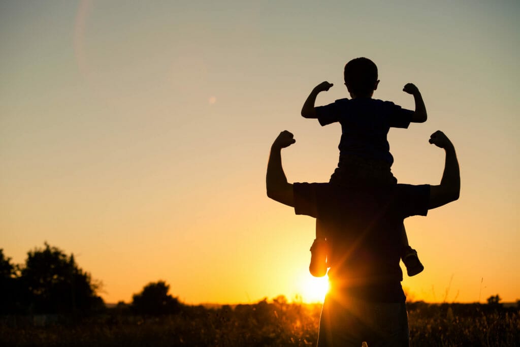 A son sits on his fathers shoulders as the play in the evening sun.